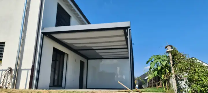 Terrasse protégée par une structure aluminium et un store vertical clair, posé devant une maison contemporaine.