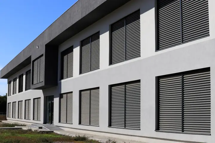 Façade contemporaine équipée de stores à lamelles extérieurs sur de nombreuses ouvertures pour contrôler la lumière et la chaleur.