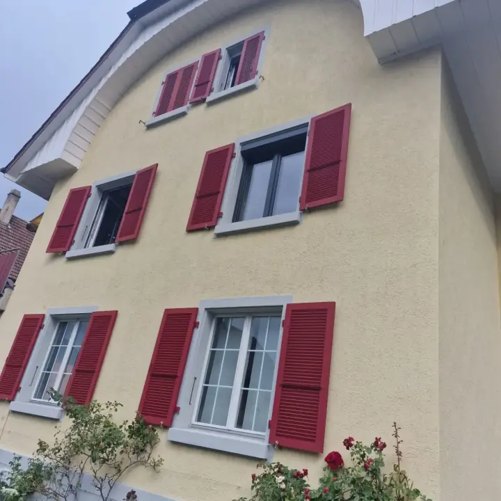 Façade résidentielle équipée de volets battants rouges sur plusieurs fenêtres.