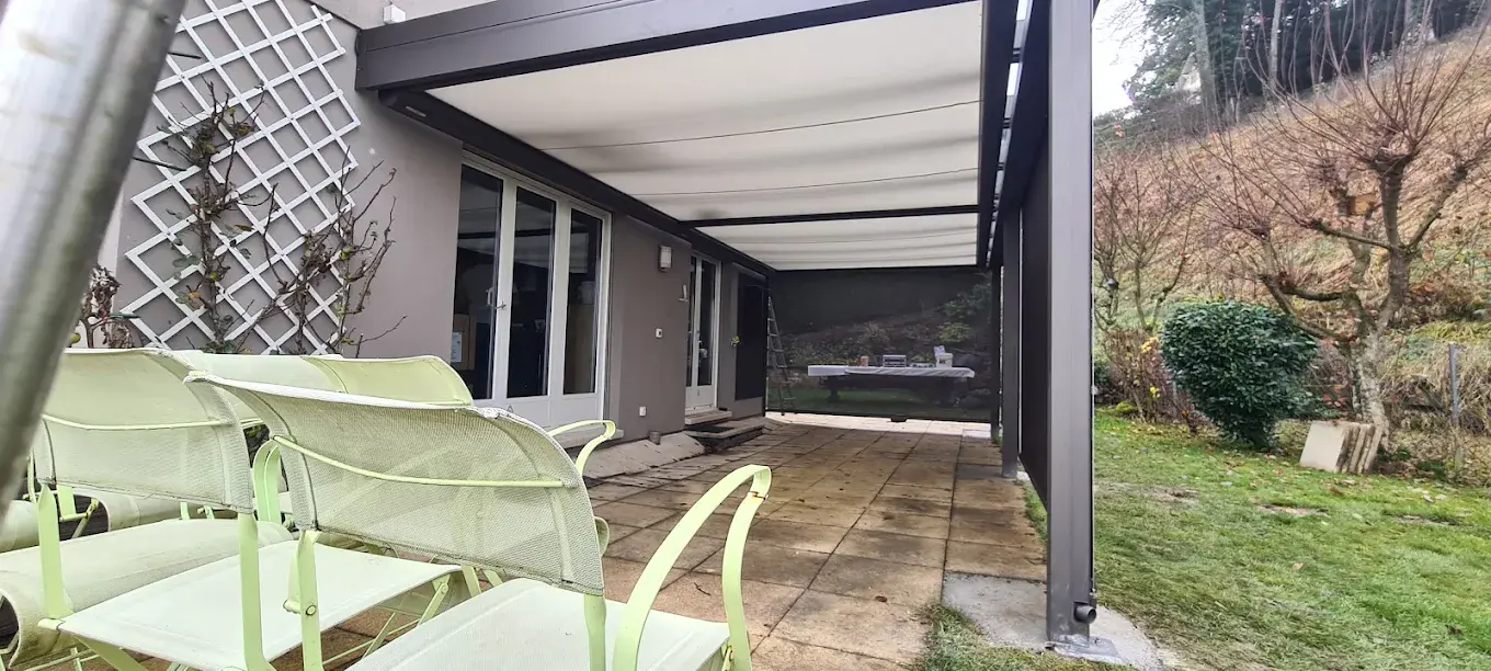 Protection de terrasse avec toile claire sous structure aluminium, couvrant un espace repas extérieur côté jardin.