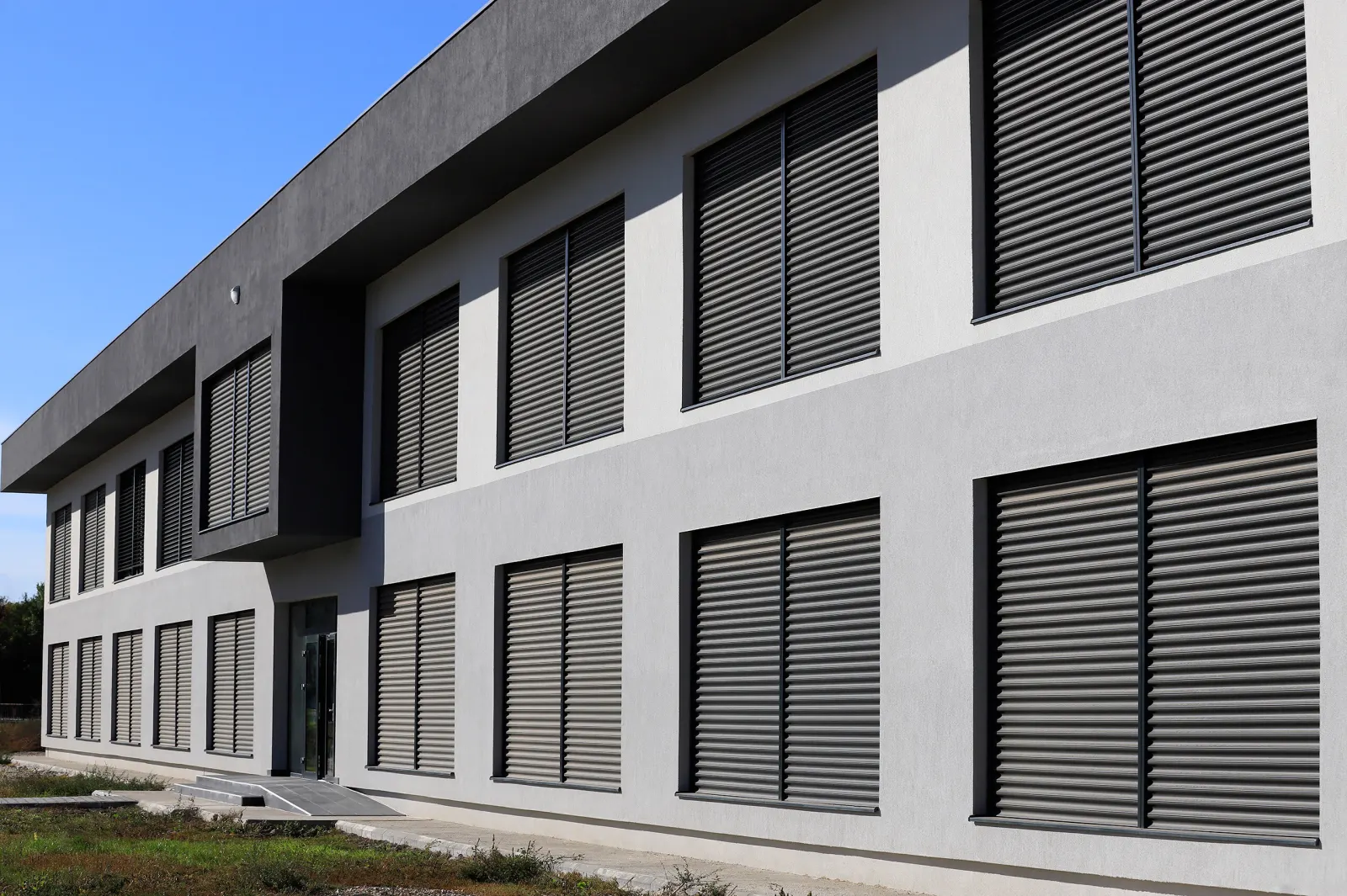 Façade contemporaine équipée de stores à lamelles extérieurs sur de nombreuses ouvertures pour contrôler la lumière et la chaleur.